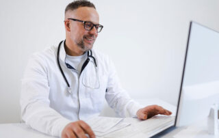 A smiling doctor checks his computer to ensure that a medical delivery is on time
