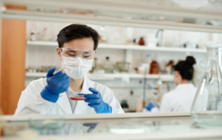 A medical scientist in a white lad coat and blue gloves works with a test sample