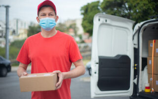 A courier in training wearing a mask, a red shirt and a red baseball cap delivers a package
