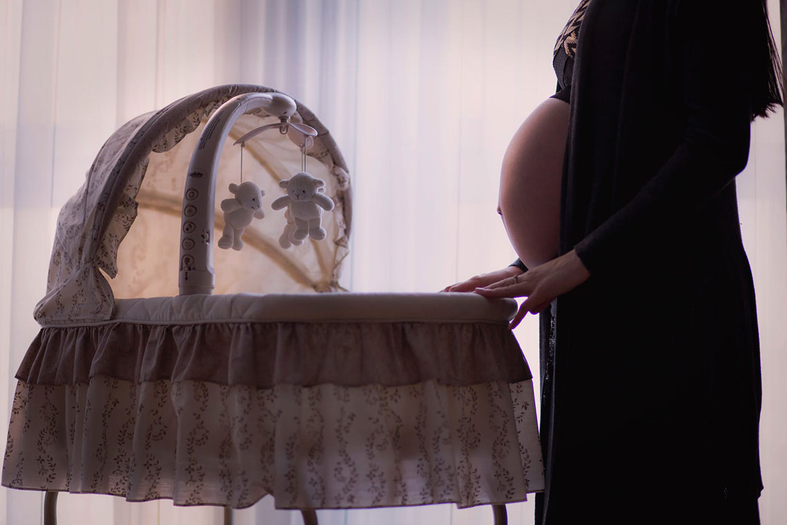 A pregnant woman standing in front of a bassinet